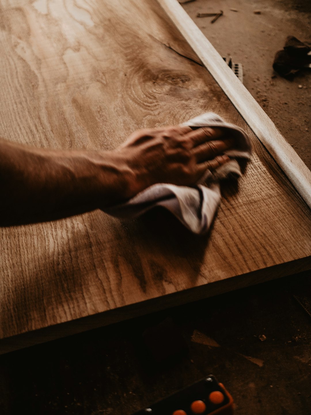 Craftsman wipes down a light-grained wooden board with a cloth.