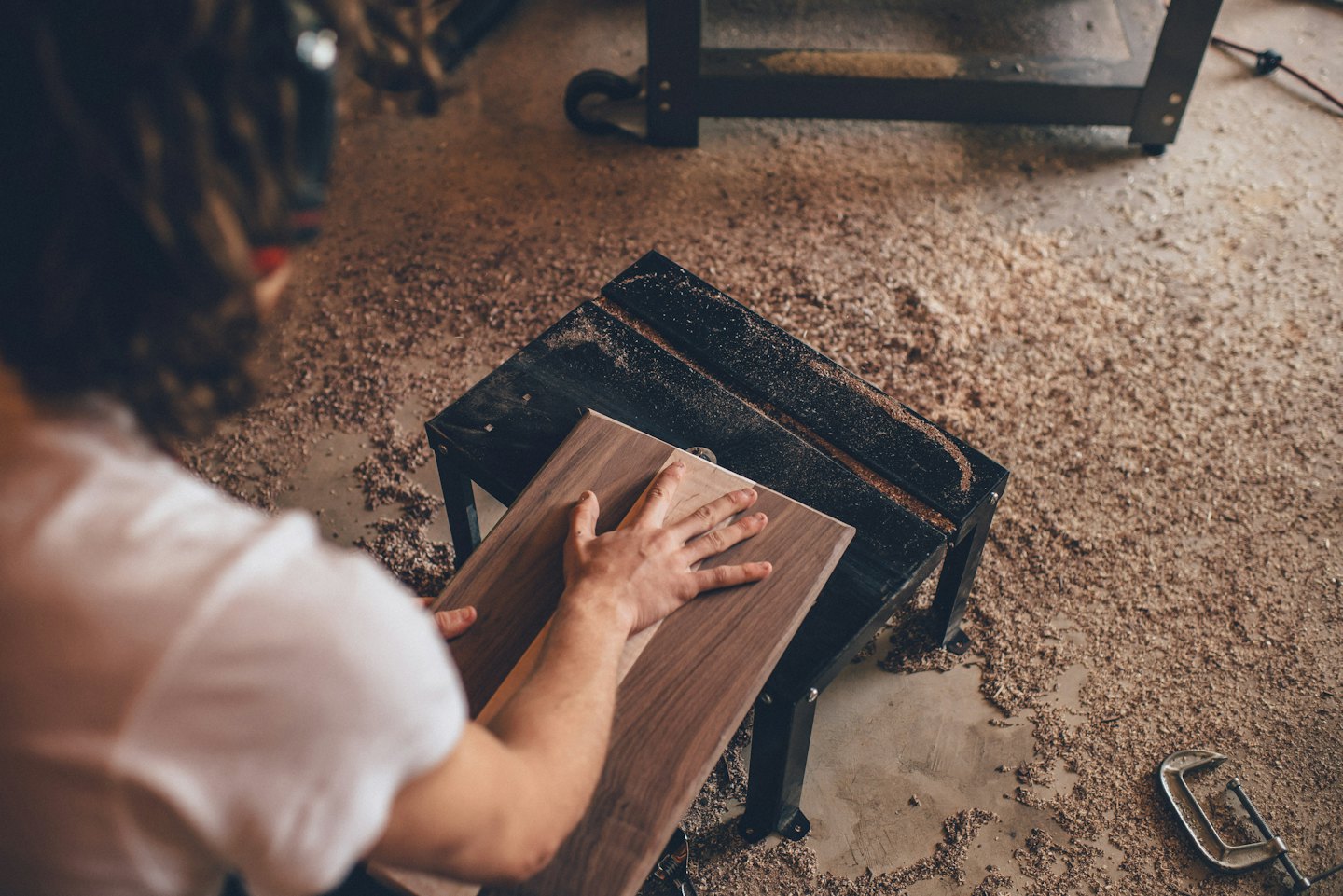 Woodworker placing wood plank on sawdust covered workbench.