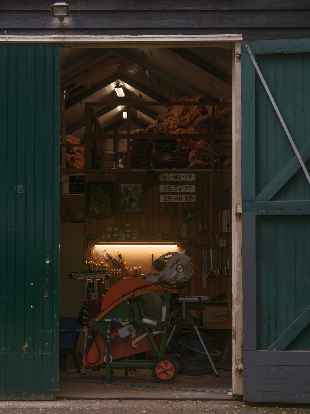 Woodworking tools and logs inside a workshop viewed through barn doors.