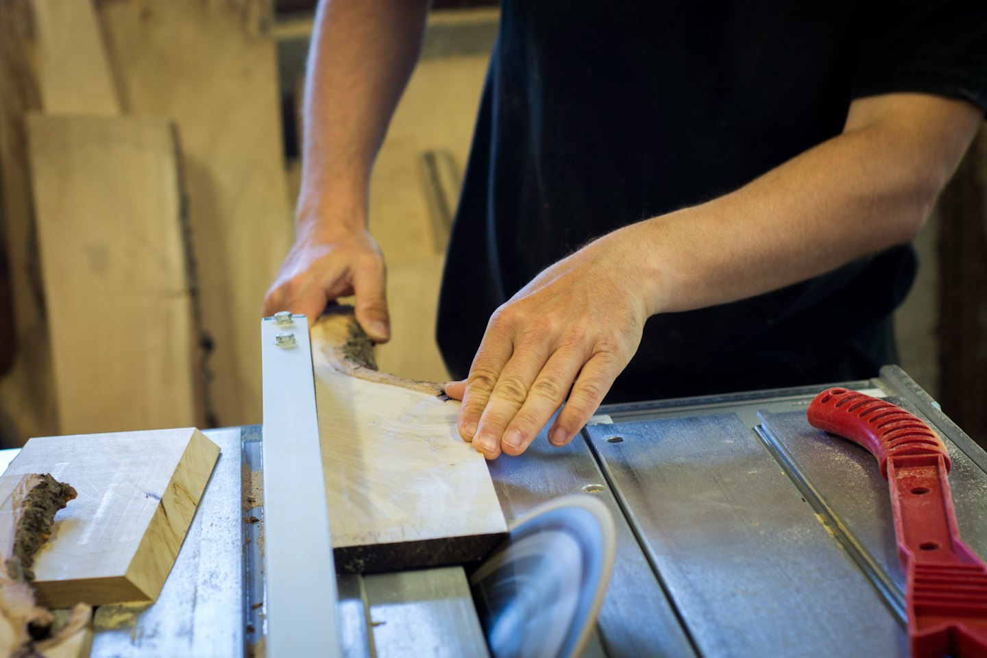 Carpenter's hands cutting wood on a table saw.